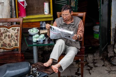 Hanoi, Vietnam - 16 Mart 2018: sokak oturan ve bir gazete okuyor yerel bir adam
