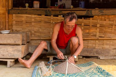 Muang Ngoi, Laos - 10 Nisan 2018: yerel adam bir el yapımı Kuzey Laos uzak bir köyde onun evinin önünde tipik Asya şapka yaptı