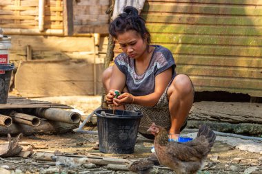 Bachong Nay,, Laos - 10 Nisan 2018: Laos bir uzak köy tavuk çevrili kendi bambu evin önünde el yıkama yapıyor yerel kadın