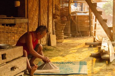 Muang Ngoi, Laos - 10 Nisan 2018: yerel adam bir el yapımı Kuzey Laos uzak bir köyde onun evinin önünde tipik Asya şapka yaptı