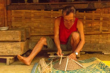 Muang Ngoi, Laos - 10 Nisan 2018: yerel adam bir el yapımı Kuzey Laos uzak bir köyde onun evinin önünde tipik Asya şapka yaptı