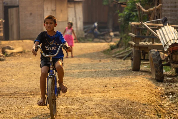 Ban Na, Laos - 10 Nisan 2018: Kuzey Laos bir uzak etnik azınlık kırsal köyde tozlu bir döşeli yolda bisiklet çocuk