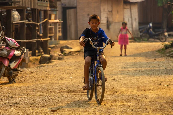 Ban Na, Laos - 10 Nisan 2018: Kuzey Laos bir uzak etnik azınlık kırsal köyde tozlu bir döşeli yolda bisiklet çocuk