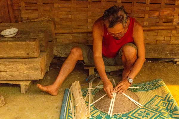 Muang Ngoi, Laos - 10 Nisan 2018: yerel adam bir el yapımı Kuzey Laos uzak bir köyde onun evinin önünde tipik Asya şapka yaptı