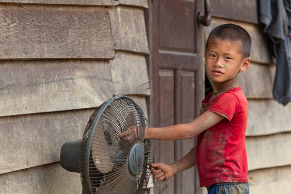 Thakhek, Laos - April 20, 2018: Ethnic minority kid touching a ventilator in front of a wooden house in a remote rural village of southern Laos