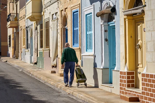 Senior maltese man walking at the street of Birzebbuga with cart