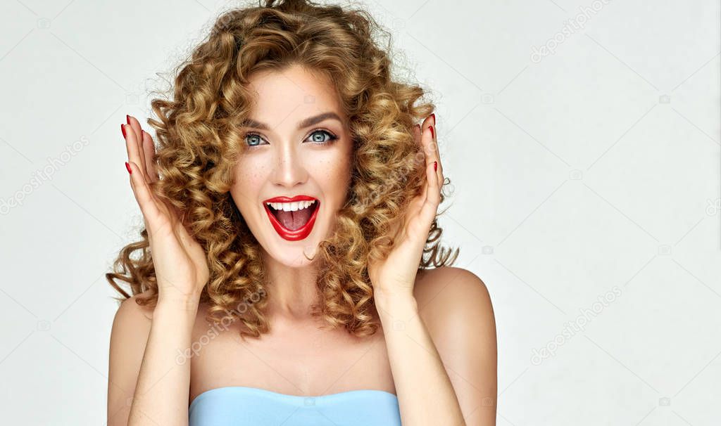 Woman with red lips and nails shouts in surprise ,and joy.Beautiful girl with curly hair surprised and shocked screaming with delight . Presenting your product. Expressive facial expressions