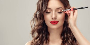 Makeup artist applies eye shadow . Beautiful woman face. Hand of visagiste, painting cosmetics of young beauty model girl . Make up in process clipart