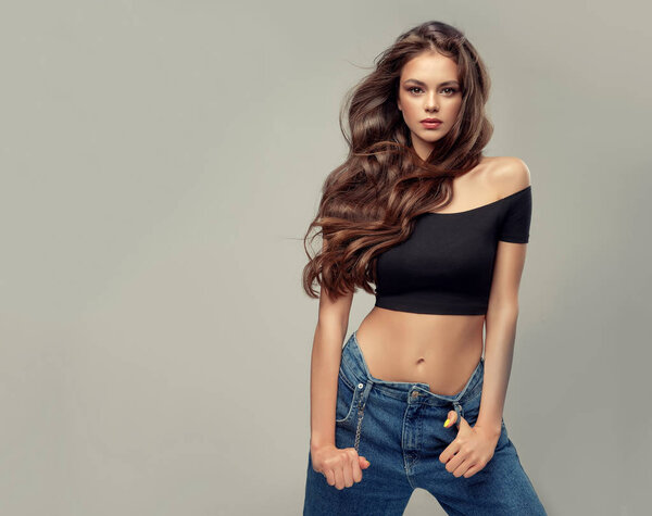 Beauty girl with long and shiny wavy hair . Beautiful woman model with curly hairstyle . Stylish sexy beautiful  woman model in  jeans hipster clothes  . girl with  is wearing trendy  denim and a short top.