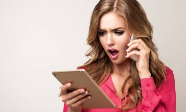 Tablet kullanan güzel bir kız reklamları ve telefonları izliyor. Çevrimiçi eğitim ya da internet üzerinden çalışma. Etkileyici yüz ifadeleri duyguları. Kadın şaşırdı ve kaşlarını çattı..