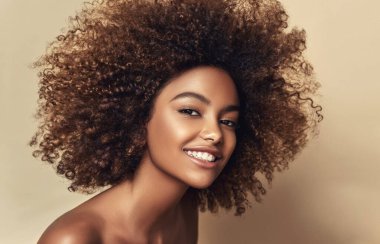 Bej arka planda temiz, sağlıklı bir teni olan Afro-Amerikan kadının güzel portresi. Cilt bakımı ve güzellik anlayışı. Gülümseyen güzel afro kız. Kıvırcık siyah saç.