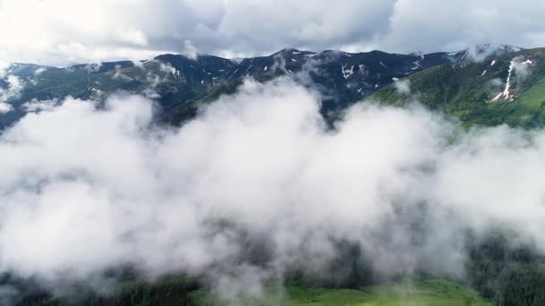 Volando a través de las nubes sobre las cimas de las montañas. Picos altos con bosque, maravilloso paisaje natural — Vídeos de Stock