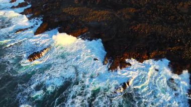 Okyanus dalgalarının yukarıdan görünüşü muhteşem kayaların ve kayalıkların etrafında köpürüyor. İlham verici ve inanılmaz doğa konsepti. Destansı sahil şeridinde güçlü deniz suyunun insansız hava aracı çekimi. Yüksek kalite 4k görüntü