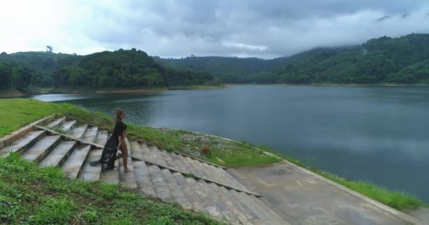 Aerial: Bella ragazza scende le scale vicino al lago e alle montagne . — Video Stock