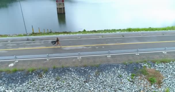 Aérea: Una hermosa chica corre a lo largo de la carretera en la presa . — Vídeo de stock