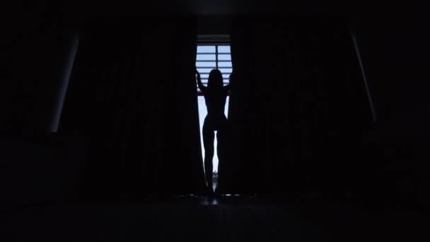 Silhouet van het mooie meisje openen de gordijnen naar het balkon. — Stockvideo