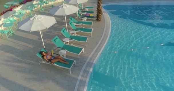 Aerial: Beautiful girl lies on a lounger by the pool. — Stock Video