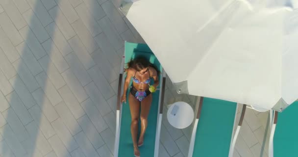 Aerial: Beautiful girl lies on a lounger by the pool and drinking a cocktail. — Stock Video