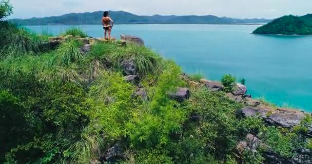 Antena: Dziewczyna stoi na szczycie góry i patrzy w dół na plaży. — Wideo stockowe