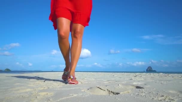 Las piernas de la chica caminando por la playa de arena blanca en un vestido rojo . — Vídeo de stock