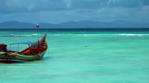 A lone traditional thai longtail boat stands on the beach with turquoise water. — Stock Video