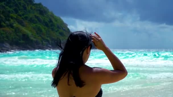 A girl is standing on the beach and looks straight in the turquoise color sea. — Stock Video