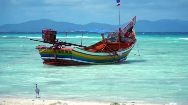 Osamělý longtail lodí stojí na pláži s tyrkysovou vodou. Pták sedí. — Stock video