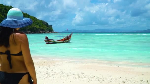 Een meisje in een hoed naar het turquoise water op het witte zandstrand. — Stockvideo