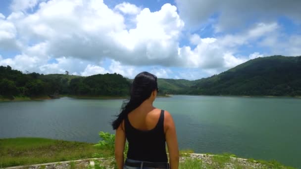 Una chica está de pie sola en el borde mirando directamente al lago con montañas — Vídeo de stock