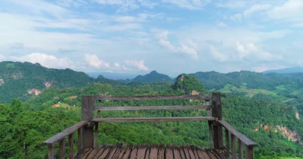 A wooden bench stands on a cliff. Mountains and a blue sky on the background. — Stock Video