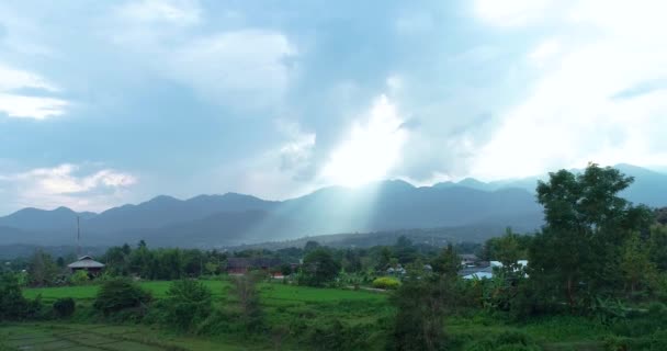 The rays of the sun are illuminate the village on a green hill near the mountains — Stock Video