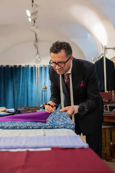 Senior male tailor choosing fabric at his atelier.