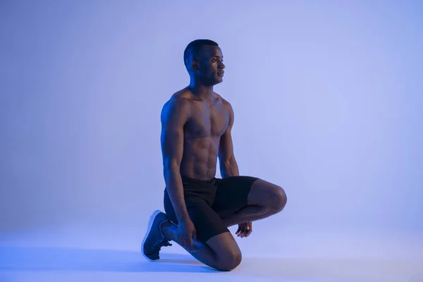 Muscular Sprinter African Man In Starting Position in blue and violet light.