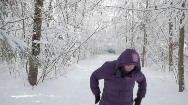 穿着冬夹克和敞篷的资深妇女在美丽的冬季森林里摇晃着雪 在阳光明媚的日子里 白雪覆盖着白色的新鲜雪 — 图库视频影像