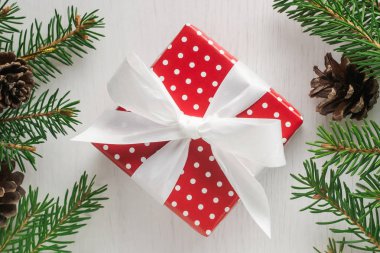 Kare Noel hediyesi beyaz lekeli ve çam çırpı ve çam kozalakları çevrili büyük beyaz yay ile kırmızı kağıt sarılı. Düz yatıyordu stili