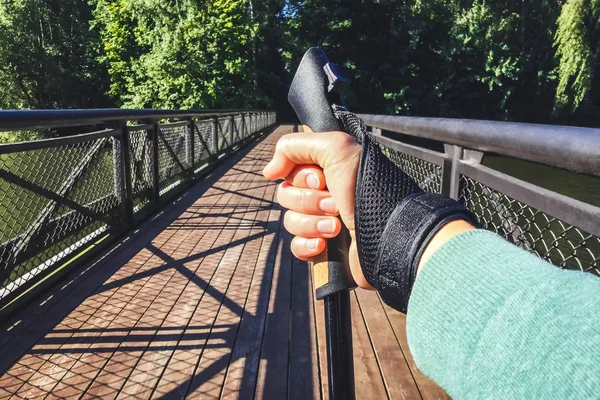 Close up of female hand holding Nordic walking pole on bridge. Concept of healthy lifestyle. Point of view shot