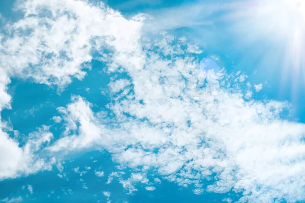 Sun beams lighting white clouds in bright blue sky. For background and wallpaper