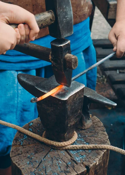 Blacksmiths forging heated metal with heavy sledgehammers against anvil on log