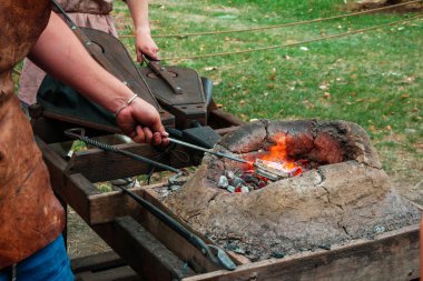 Ateş yakmak için demirci yanan kömürlerin Ortaçağ fırınında alay ve körüklü sıkma eski giysiler içinde. Yeniden yapılanma