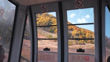 Sochi, Rosa Khutor, Rusya Federasyonu - 13 Ekim 2017: sarı ve kırmızı sonbahar ağaçlar dağ yamacında, füniküler kabin pencere güneşli günde bakarak insanlar