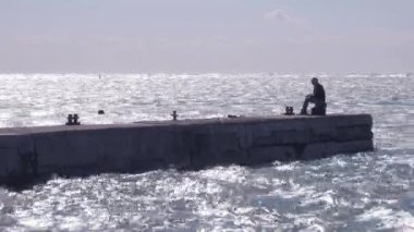 Balıkçı balıkçılık çubuk üzerinde eski iskelesi sahil'rüzgarlı gün eğirme ile silüeti