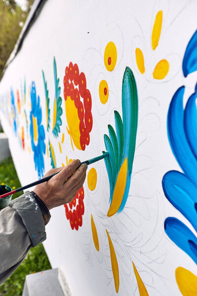 The artist paints with oil paints on a white wall.