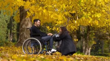Tekerlekli sandalyedeki adam ve kız arkadaşı bir sonbahar günü parktalar.