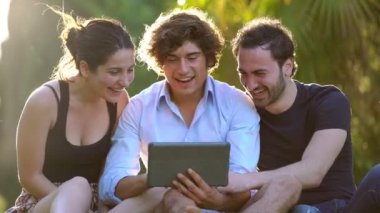 Mutlu arkadaş grubu çimenlikte tablet kullanıyor- yavaş çekim