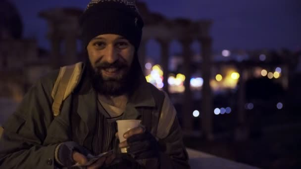 lächelnd zeigt ein glücklicher Obdachloser in der Nacht seine Almosen