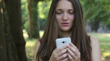 Smartphone park ve gülümseyerek kameraya kullanan mutlu genç kadın