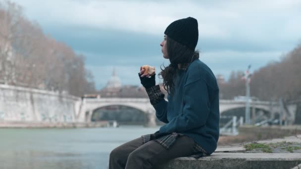 孤独的无家可归的年轻女子吃着一个凝视着河水的苹果 — 图库视频影像