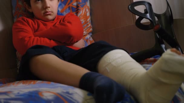 彼の寝室で一人で足の石膏で怒っている悲しいキッド — ストック動画