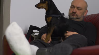 Olgun adam kanepede kırık bir bacak ile köpek okşadı
