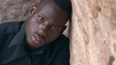 Üzgün yalnız genç siyah göçmen kameraya bakarak duvara yaslanmış